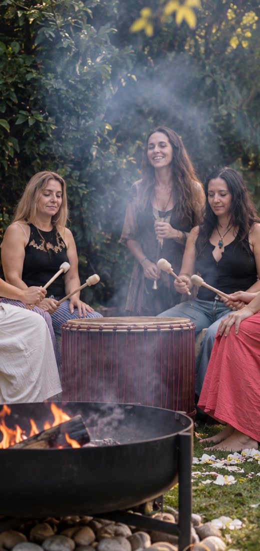 Women drumming around an open fire at dusk