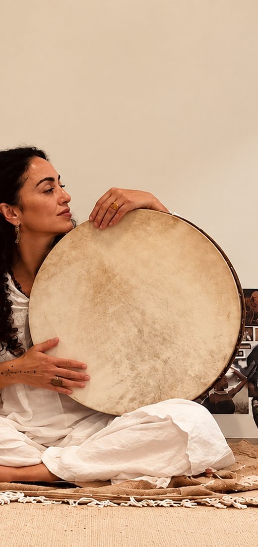 A woman playing a frame drum in a room full of morning light