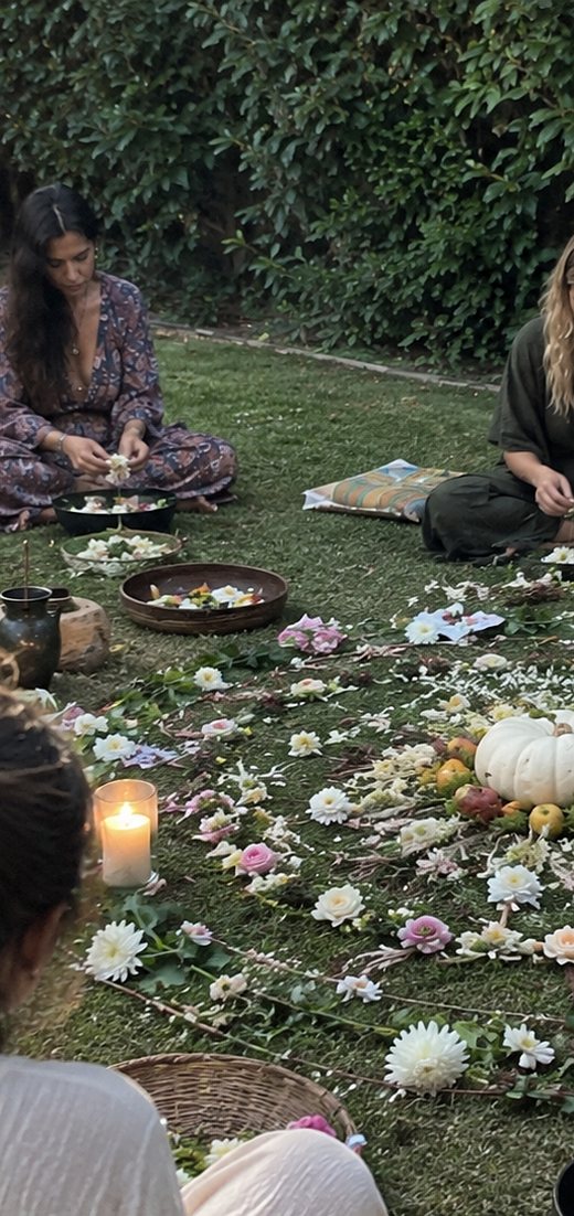 Women kneeling to build a mandala of petals and white pumpkins on the grass